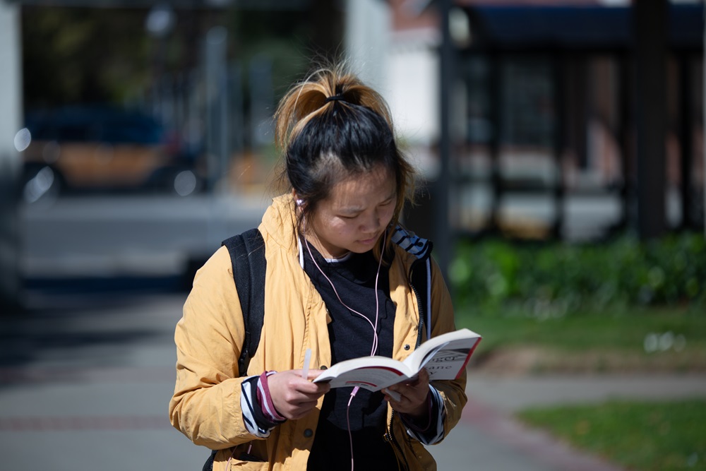 Student reads a book while walking at Sacramento City Campus. 