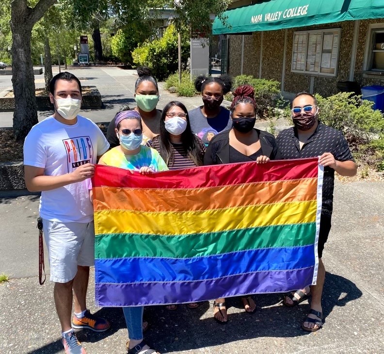 Group of students facing camera holding a rainbow flag