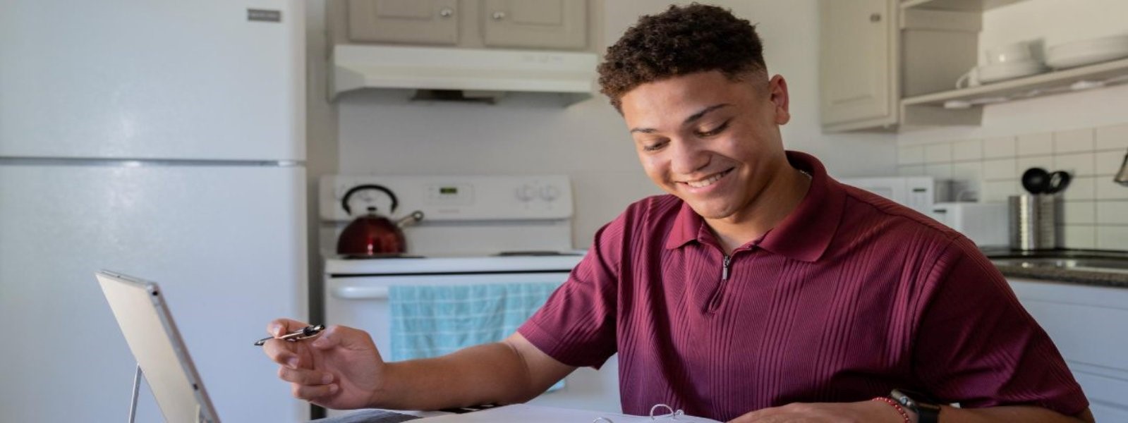 student sitting at table in kitchen in front of open laptop, smiling