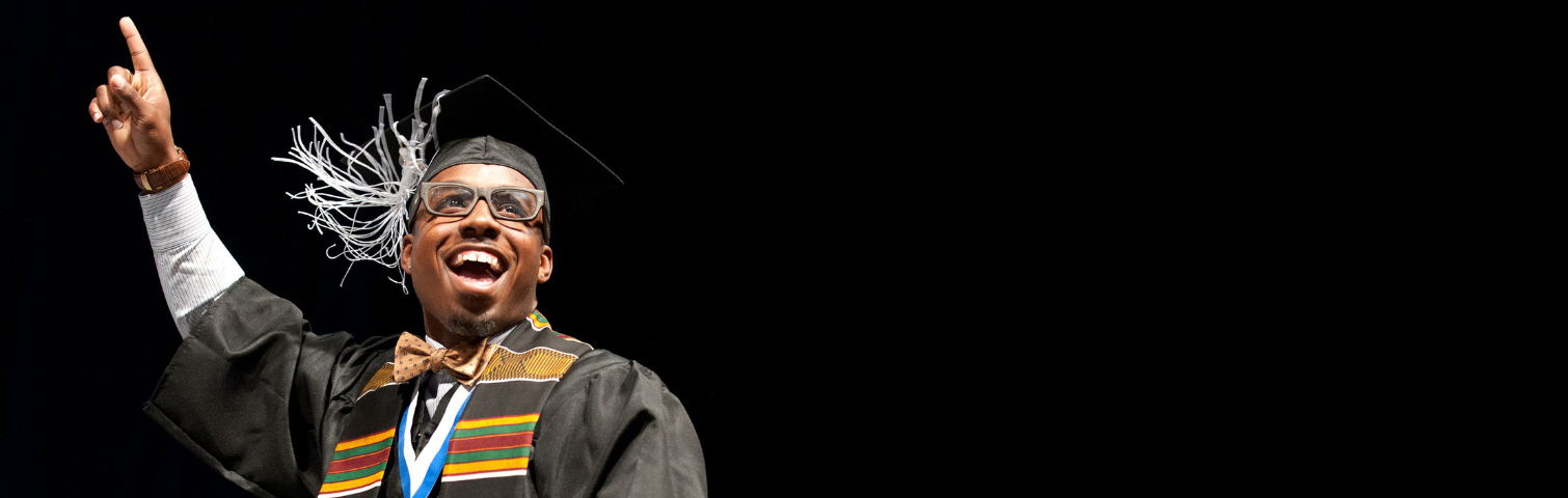 photo of a male-appearing person weraing a graduation cap and gown and graduation scarfs smiling and waving