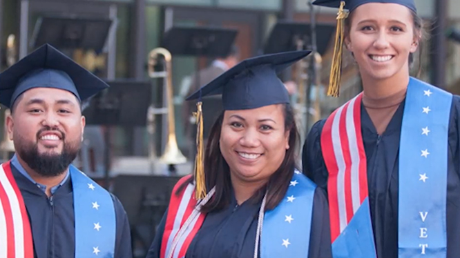 Photo of veteran graduates with caps and gowns and flags