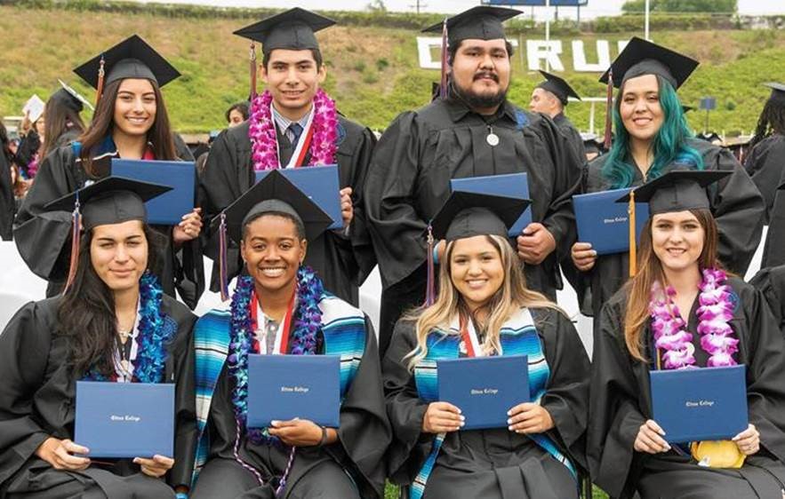 Eight students in two horizontal rows holding diplomas