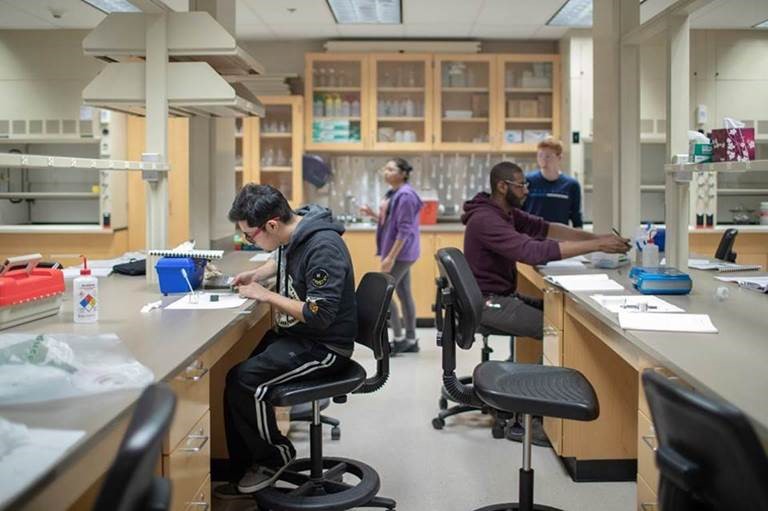 chemistry lab classroom with two students sitting at lab tables and two students standing