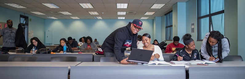 Person standing next to person sitting with a laptop at a table