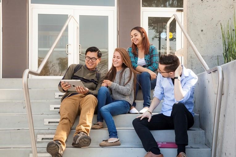 four students sitting on steps looking at a laptop