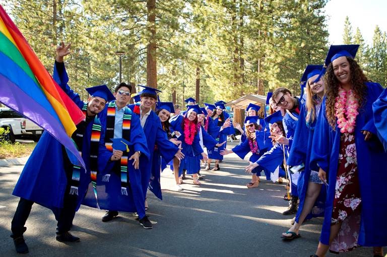 Photo of two rows of graduates in blue caps and gowns and a rainbow flag
