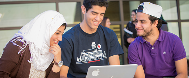 three people outside with a laptop laughing