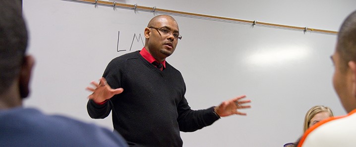 Black African American Professor facing class with back to a white board with two students facing front