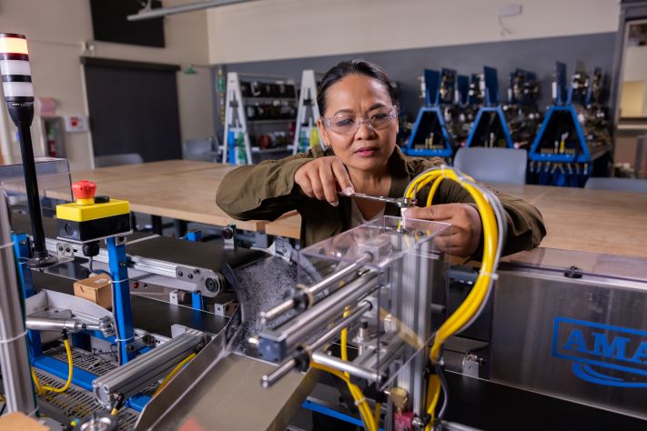 A female California community college student works on a piece of machinery