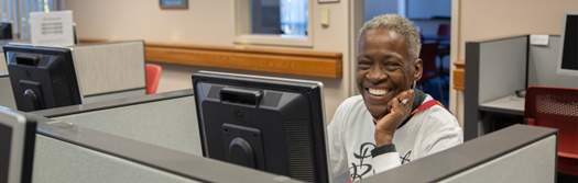 Photo of person in front of a computer monitor sitting and smiling